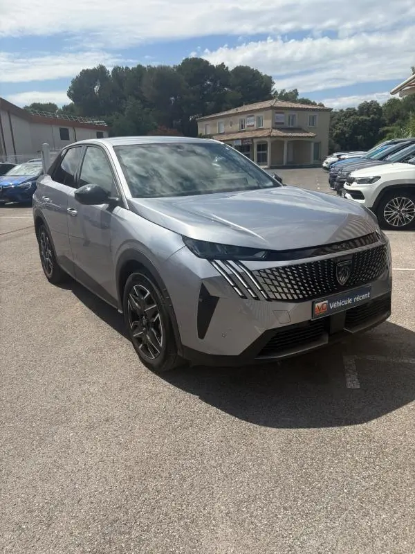 Peugeot 3008 Hybrid gris clair en 3/4 avant droit, avec calandre distinctive et phares LED fins, stationné en extérieur.