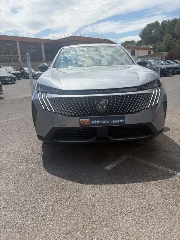 Vue de face du Peugeot 3008 Hybrid gris clair 2025 avec calandre noire et feux LED en forme de griffes.