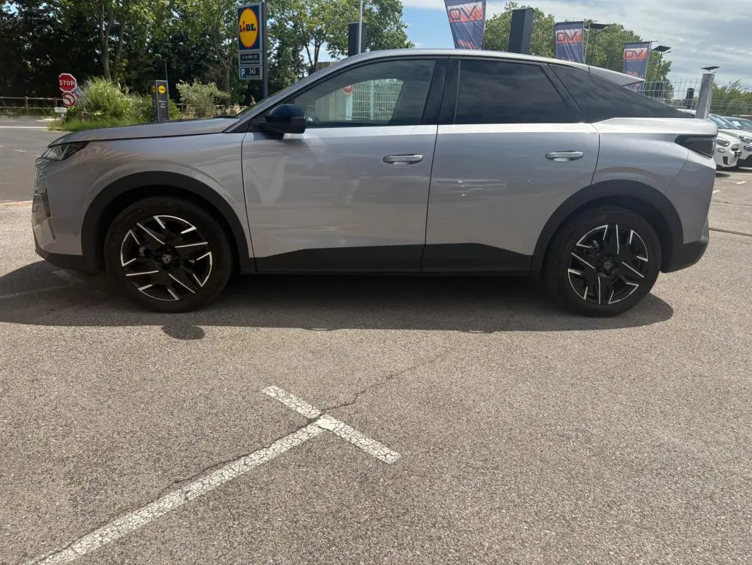 Vue de profil côté gauche d’un Peugeot 3008 Hybrid gris clair 2025 avec jantes noires et toit noir contrasté.