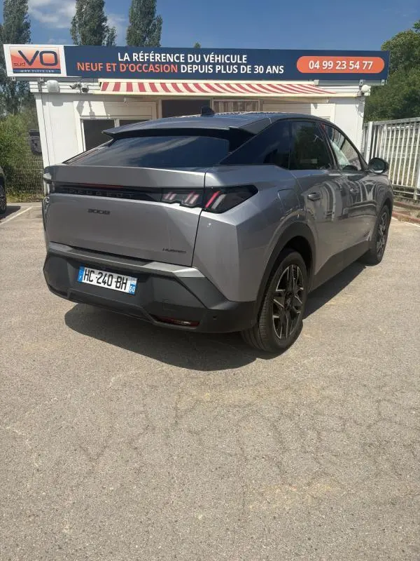 Vue 3/4 arrière droite d'un Peugeot 3008 Hybrid gris clair 2025 avec feux arrière distinctifs et toit noir.