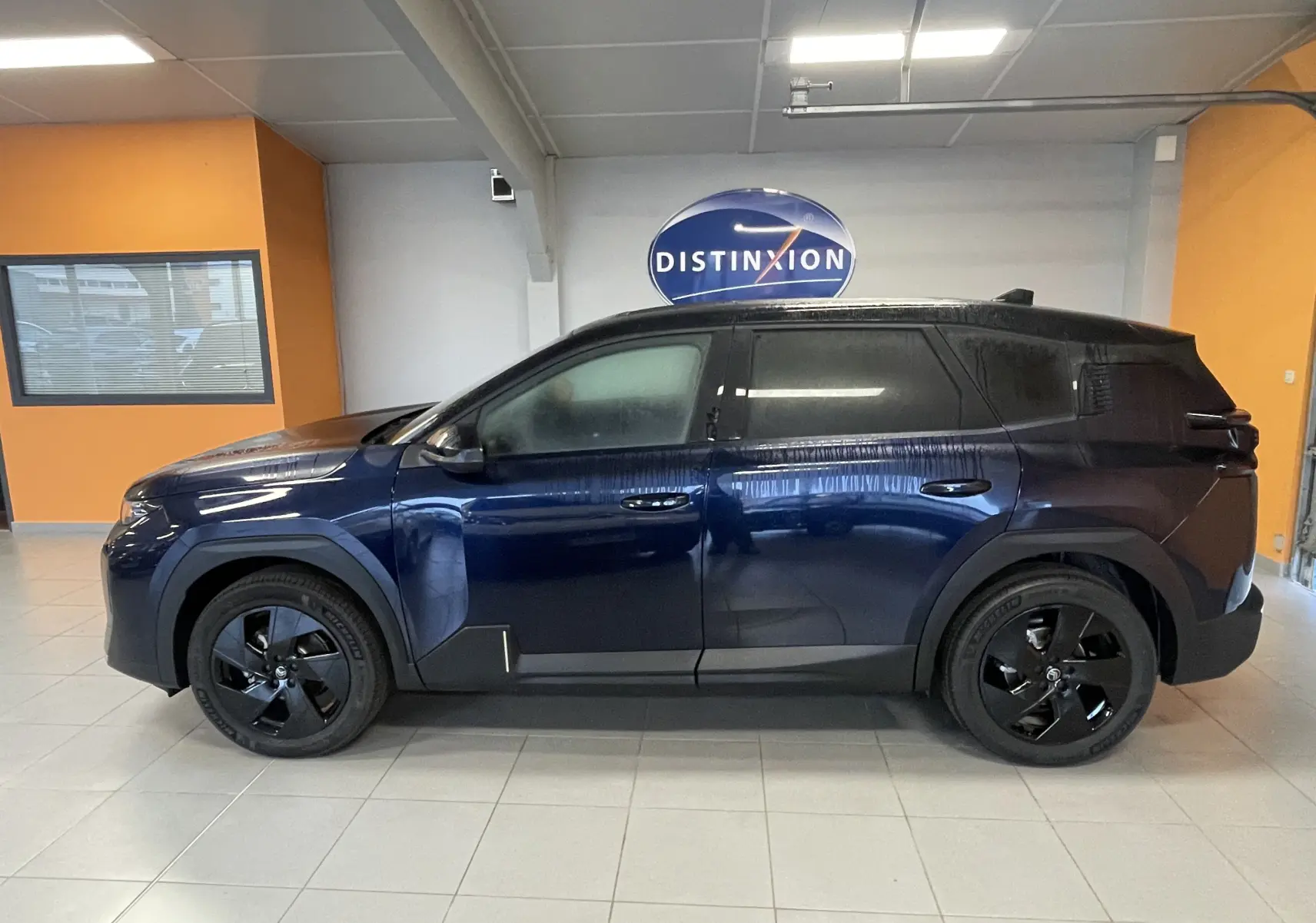 Profil côté gauche du Citroën C5 Aircross hybride 2026 bleu Eclipse avec toit noir et jantes noires en intérieur showroom.
