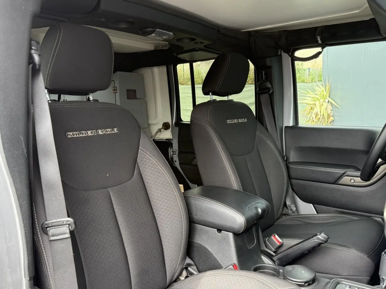 Vue intérieure avant des sièges noirs du Jeep Wrangler Golden Eagle avec accoudoir central et ceintures visibles.