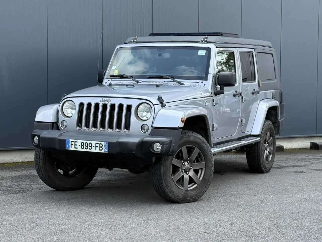 Jeep Wrangler 2.8 CRD 2019 Billet Silver en 3/4 avant droit, avec toit relevable et stickers sur capot.