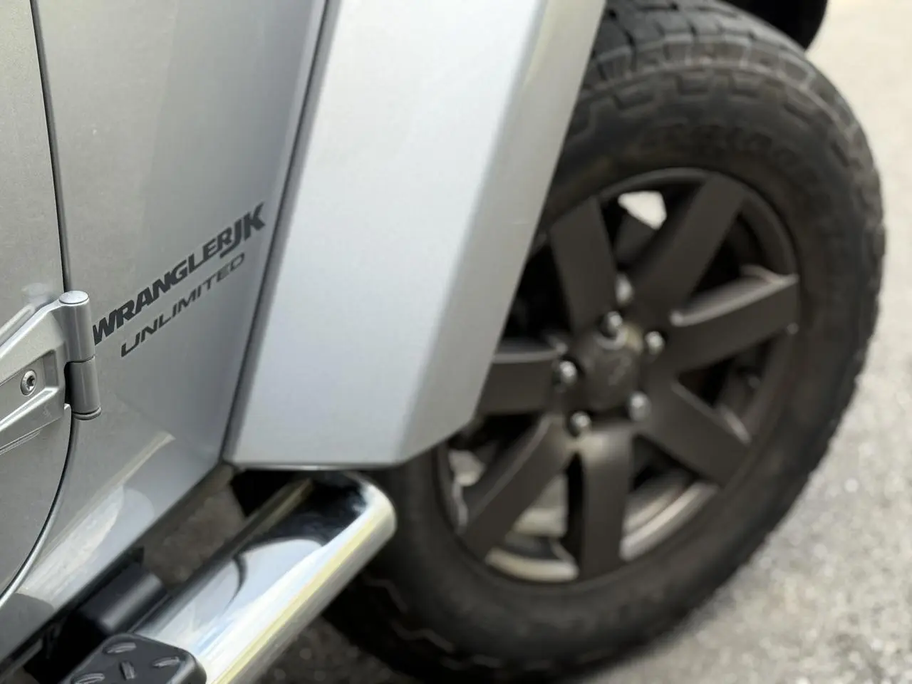 Gros plan sur la roue arrière droite et la portière argentée du Jeep Wrangler JK Unlimited avec logo visible.