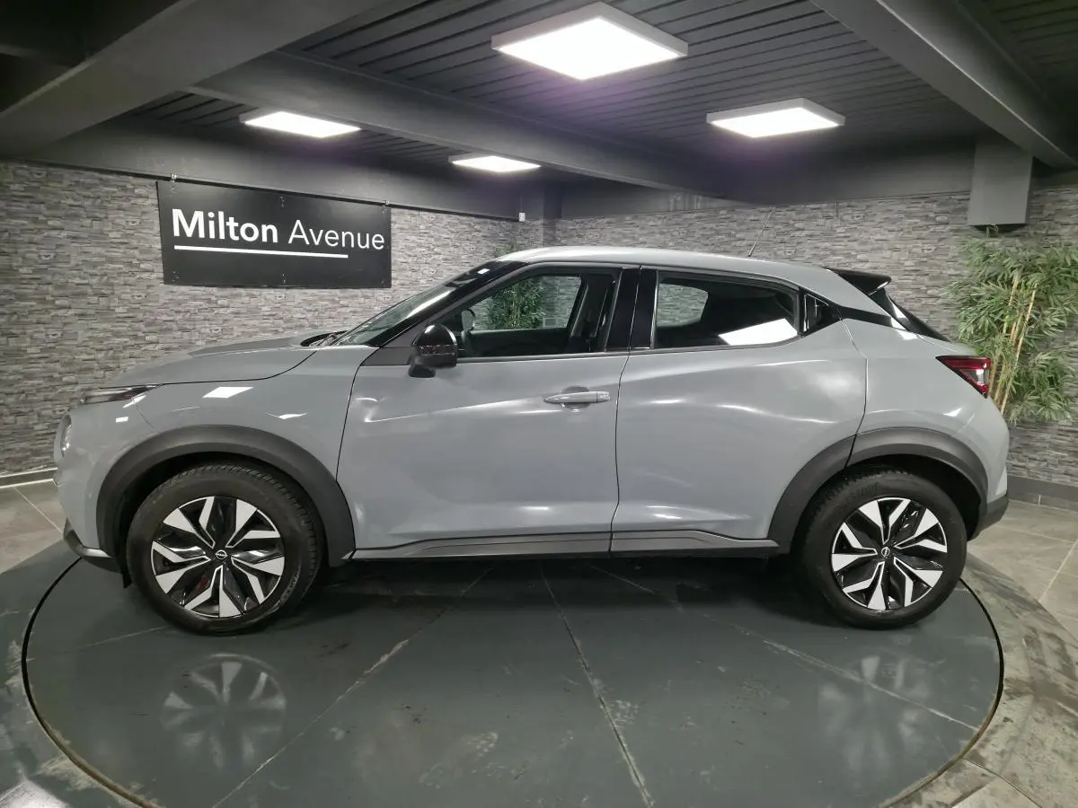 Profil côté gauche du Nissan Juke gris métallisé 2023 avec jantes bi-ton et poignées de porte couleur carrosserie.