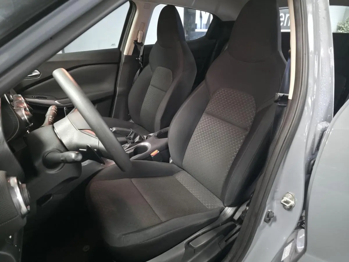 Vue intérieure côté conducteur du Nissan Juke gris 2023, mettant en valeur les sièges tissu noir et le volant réglable.