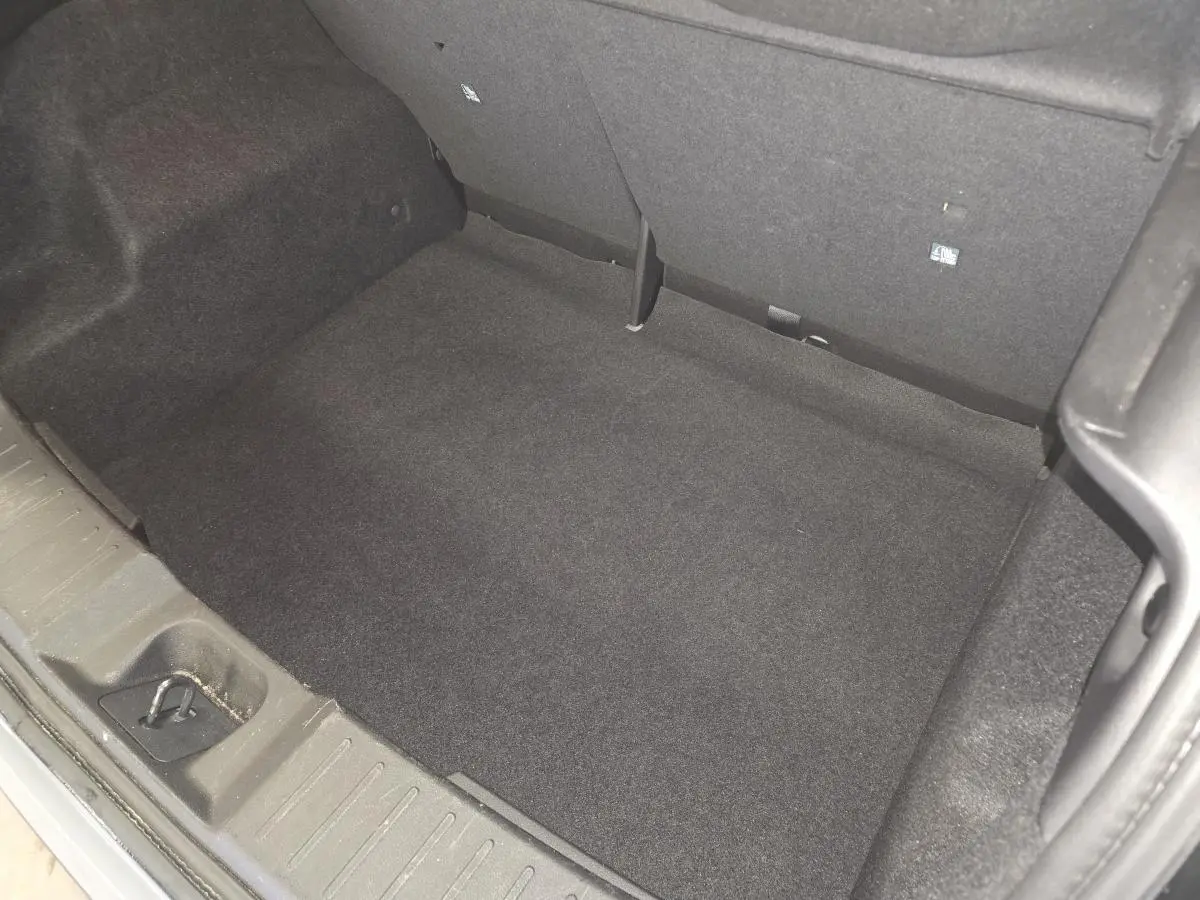 Coffre vide vu de dessus du Nissan Juke gris 2023, montrant la moquette noire et les fixations ISOFIX arrière.