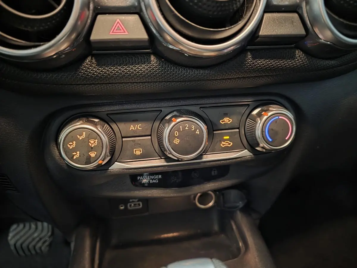 Gros plan sur les commandes de climatisation manuelle noires du Nissan Juke 2023 avec boutons éclairés orange et bleu.