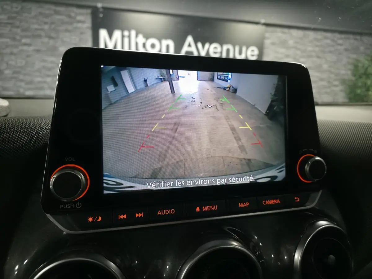 Écran tactile du Nissan Juke 2023 montrant la caméra de recul avec guidage coloré dans un garage.