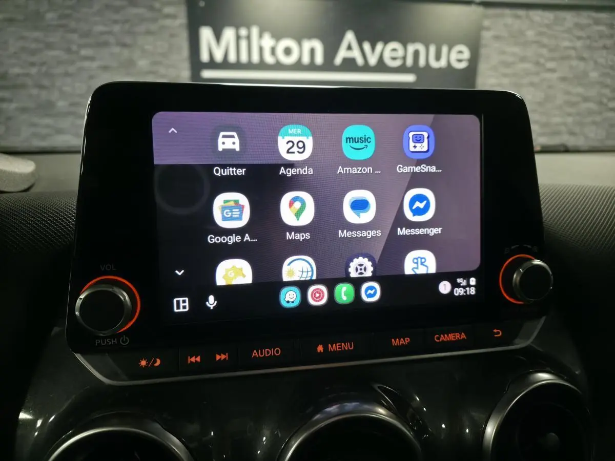 Écran tactile central du Nissan Juke 2023 affichant des applications de navigation et communication, avec commandes audio en dessous.
