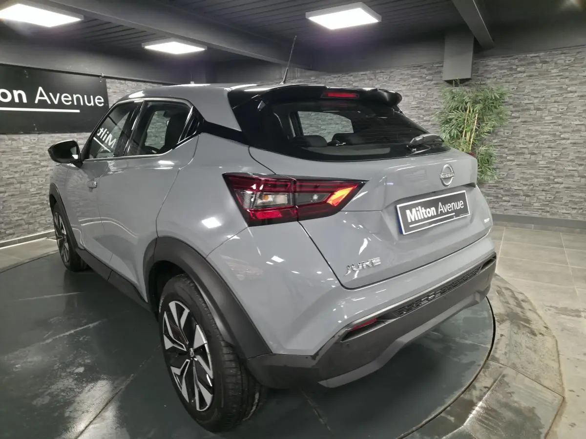 Nissan Juke gris métallisé vu en 3/4 arrière droit, avec feux LED et jantes bi-ton 17 pouces dans un showroom.