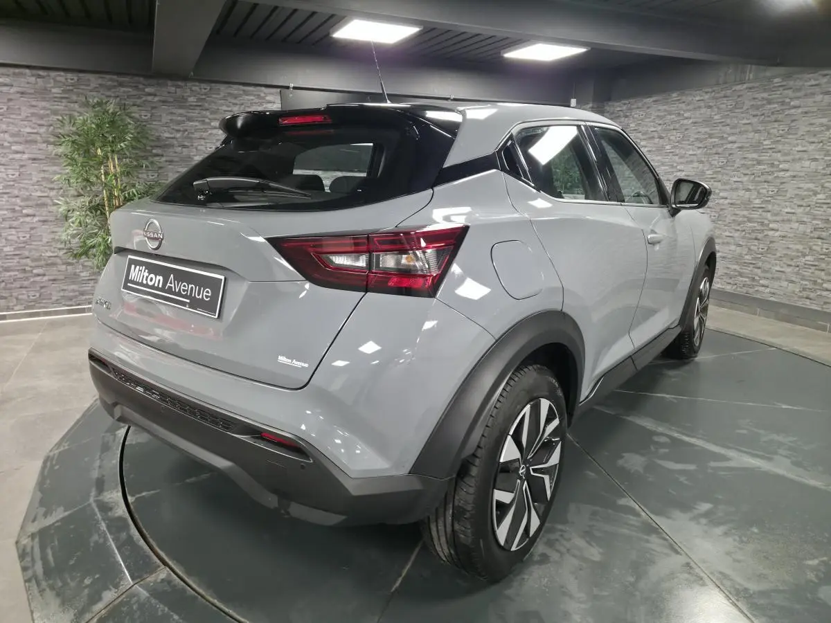 Nissan Juke gris métallisé vue 3/4 arrière droit, avec jantes bi-ton et feux arrière LED dans un showroom.