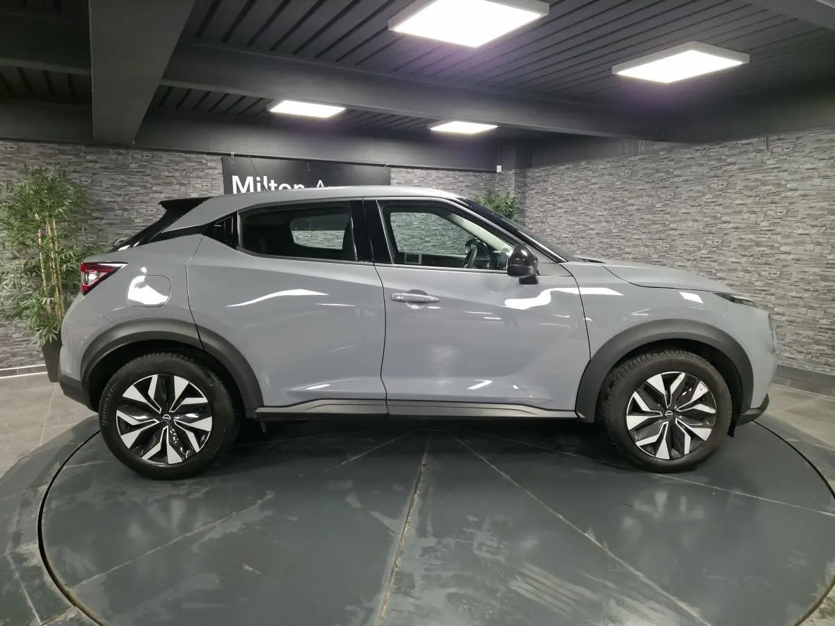 Profil côté droit du Nissan Juke gris 2023 avec jantes bi-ton et coques de rétroviseurs noires en showroom.