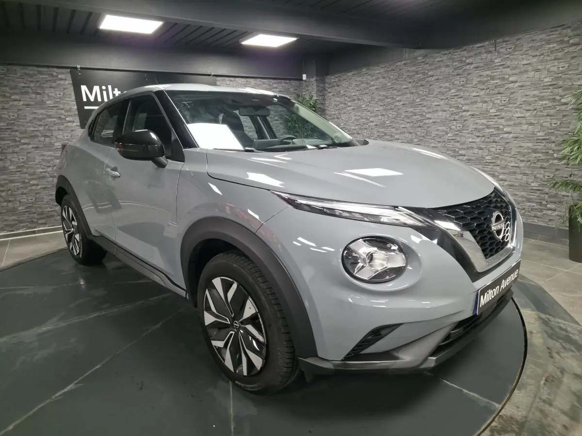 Nissan Juke gris métallisé vu en 3/4 avant droit, avec calandre noire et jantes bi-ton en intérieur showroom.