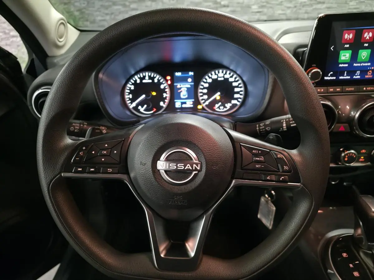 Vue intérieure centrée sur le volant noir Nissan Juke 2023 avec tableau de bord et écran tactile en arrière-plan.