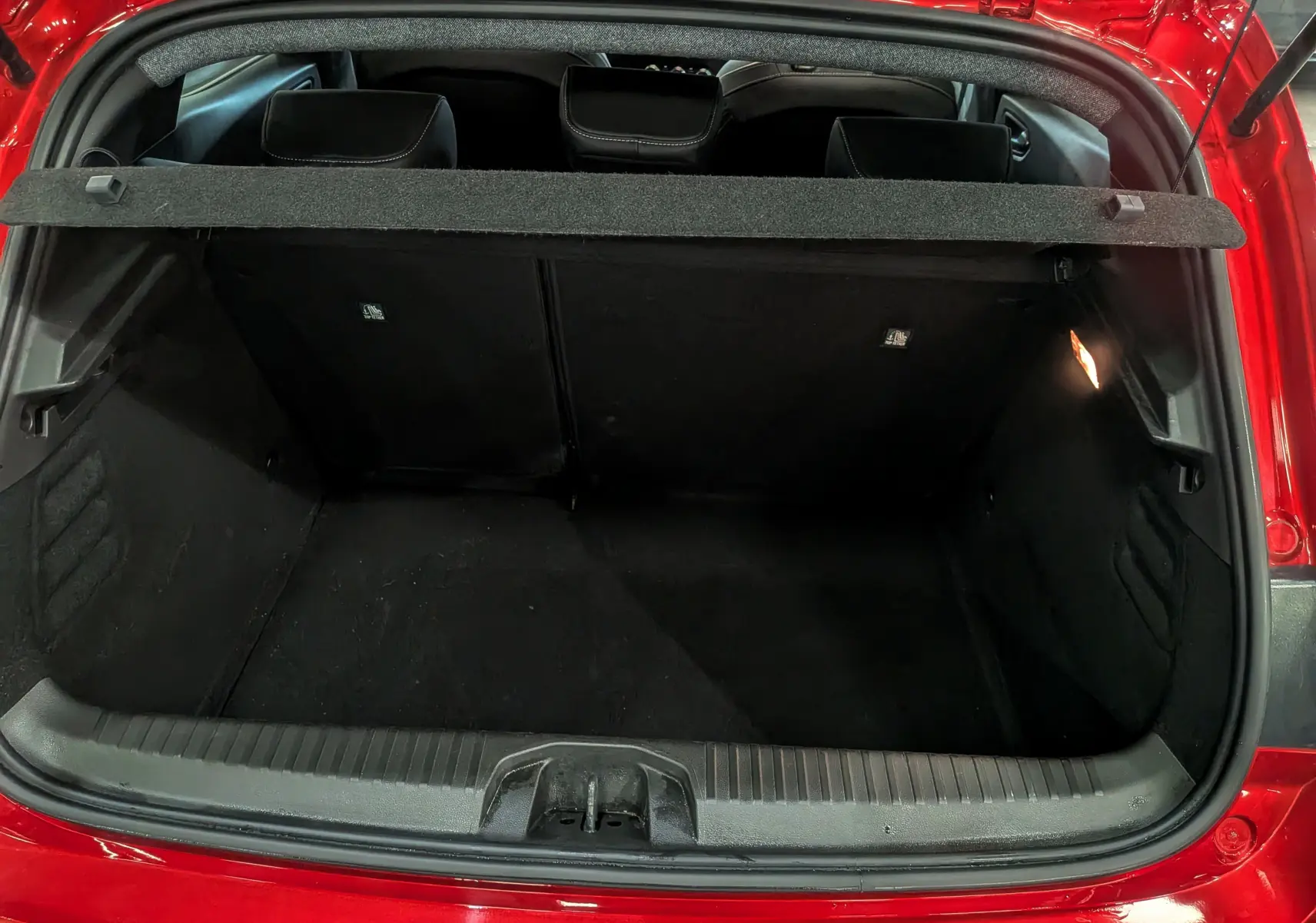 Coffre ouvert vu de l'arrière d'une Renault Clio V Rouge Flamme, montrant l'espace de chargement vide et la plage arrière.