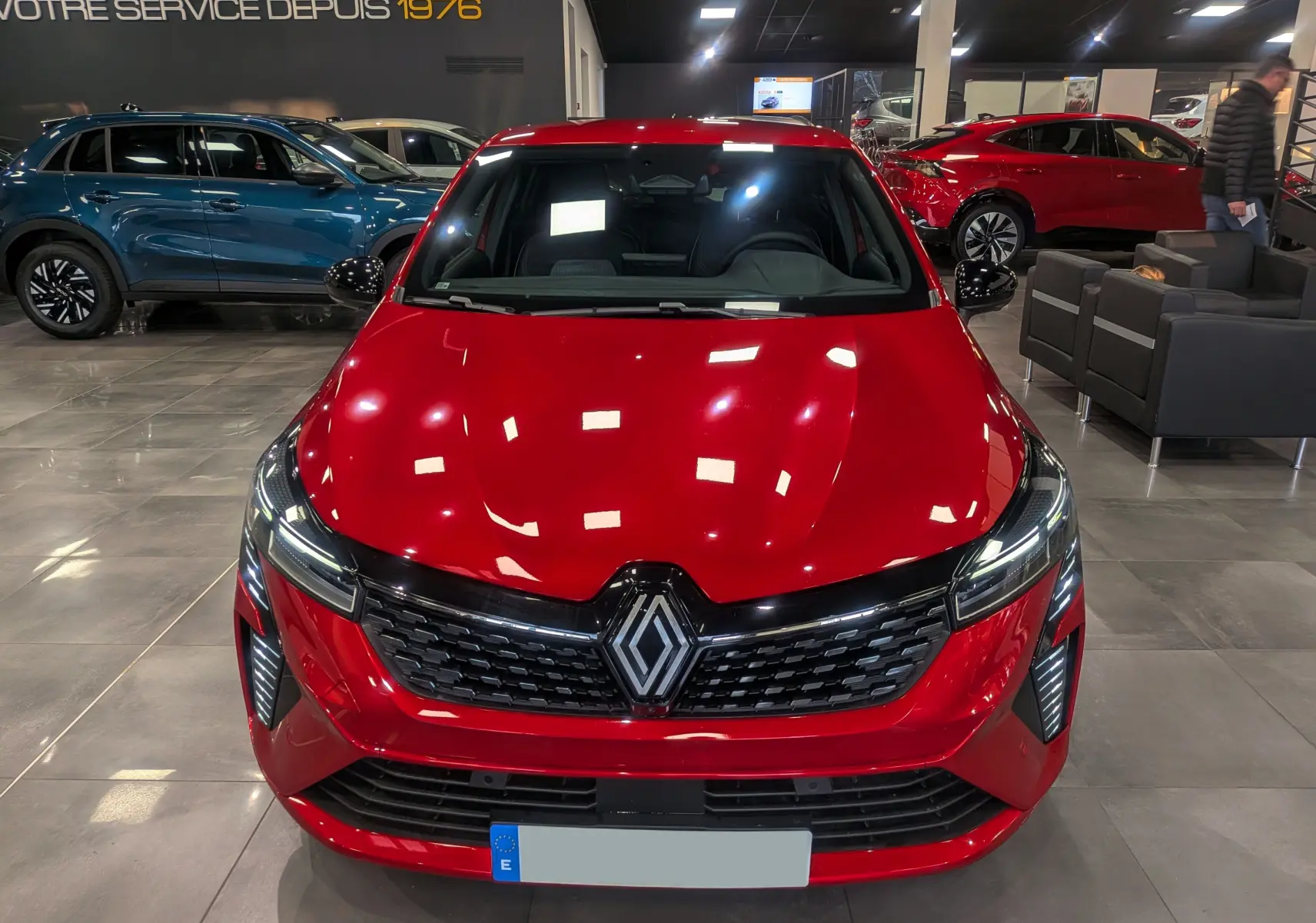 Vue avant d'une Renault Clio V rouge flamme en showroom, mettant en valeur la calandre noire et les phares LED distinctifs.