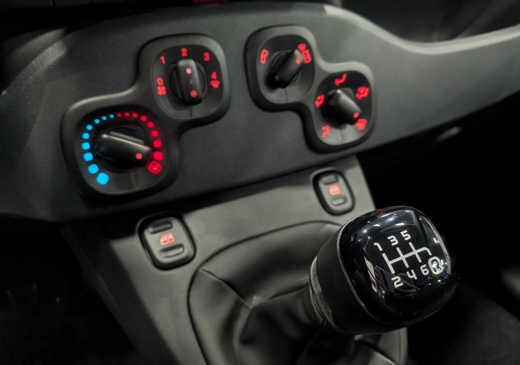 Gros plan sur le levier de vitesses manuel 6 rapports et les commandes de climatisation du tableau de bord de la Fiat Panda.