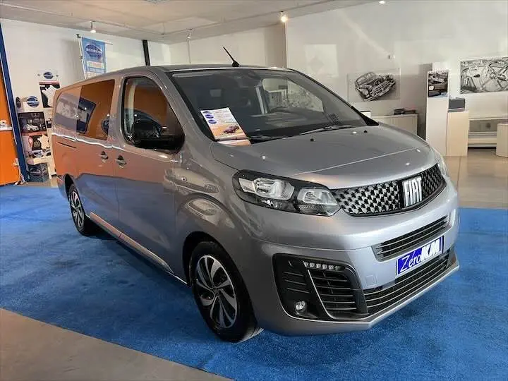 Vue 3/4 avant droite du FIAT Scudo cabine approfondie gris Artense métal exposé en showroom avec calandre distinctive et jantes modernes.