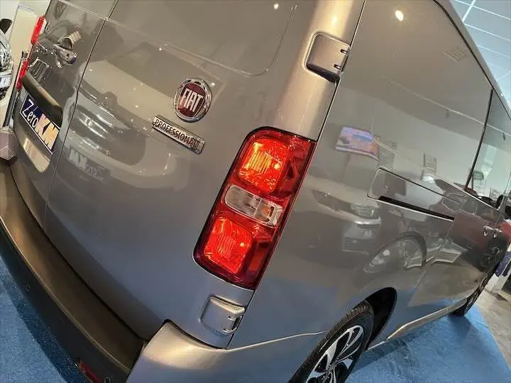 Vue 3/4 arrière droite d'un FIAT Scudo gris Artense métallisé avec feux arrière allumés en showroom.