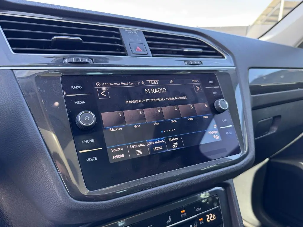 Écran tactile central du tableau de bord du Volkswagen Tiguan 2.0 TDI gris, affichant la radio FM en intérieur lumineux.