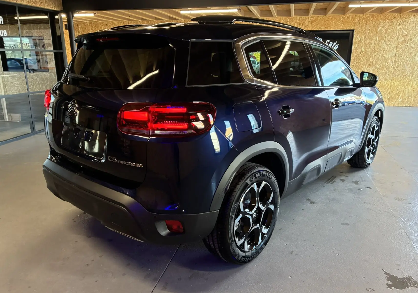 Vue 3/4 arrière droite du Citroën C5 Aircross bleu Eclipse Metal avec feux LED et jantes bicolores en intérieur showroom.
