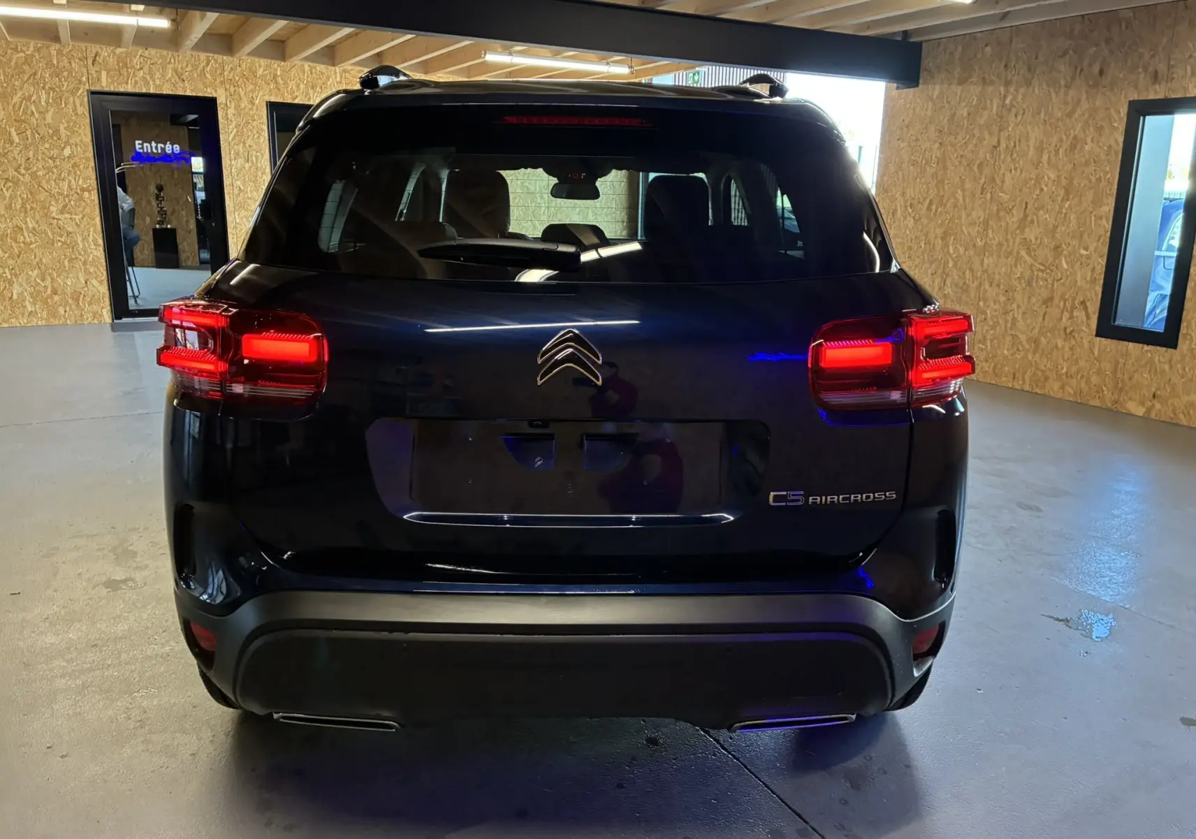 Vue arrière d'un Citroën C5 Aircross bleu Eclipse Métal avec feux arrière allumés dans un garage.