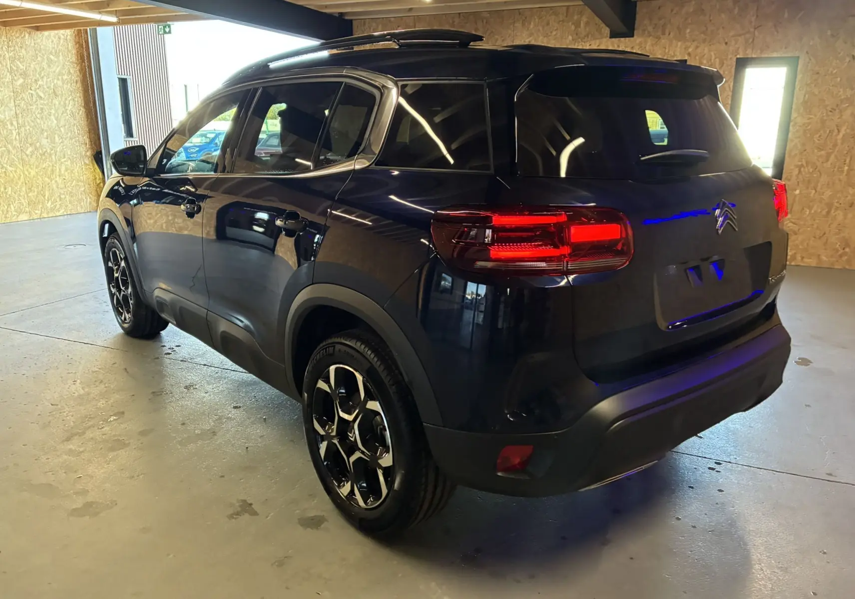 Vue 3/4 arrière droite du SUV Citroën C5 Aircross bleu Eclipse Metal avec jantes noires et feux arrière allumés dans un garage.