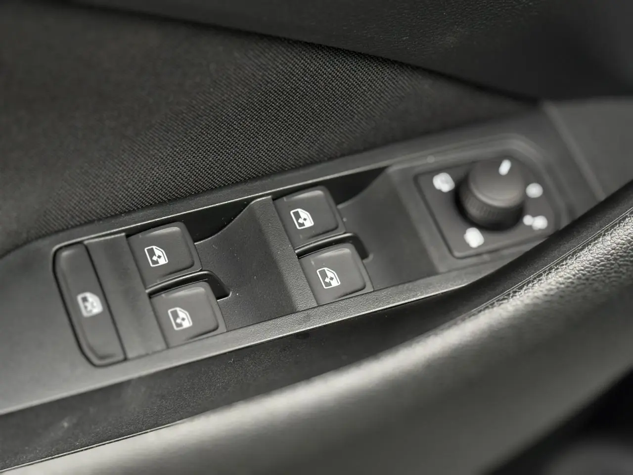 Gros plan sur les commandes de lève-vitres et réglage des rétroviseurs côté conducteur du Skoda Kamiq gris argent 2025.