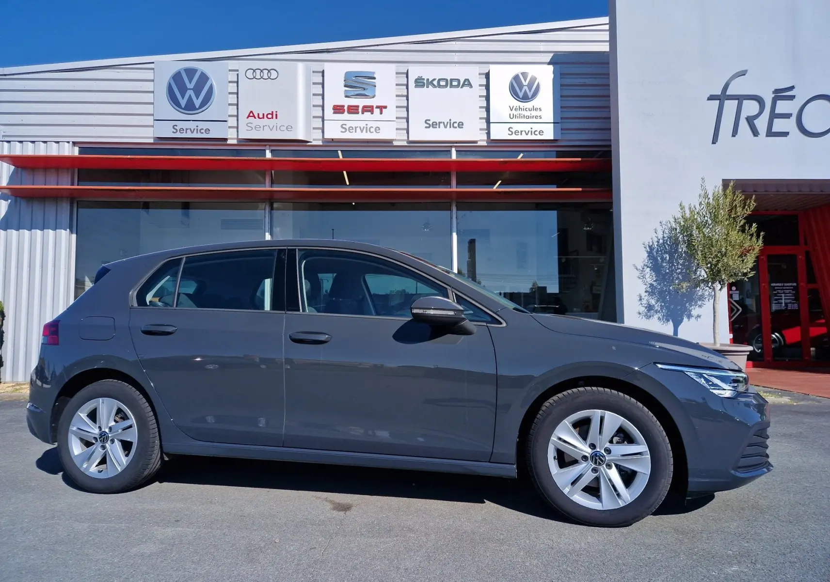 Profil côté gauche d'une Volkswagen Golf A8 2.0 TDI gris Urano garée devant un service multimarques.