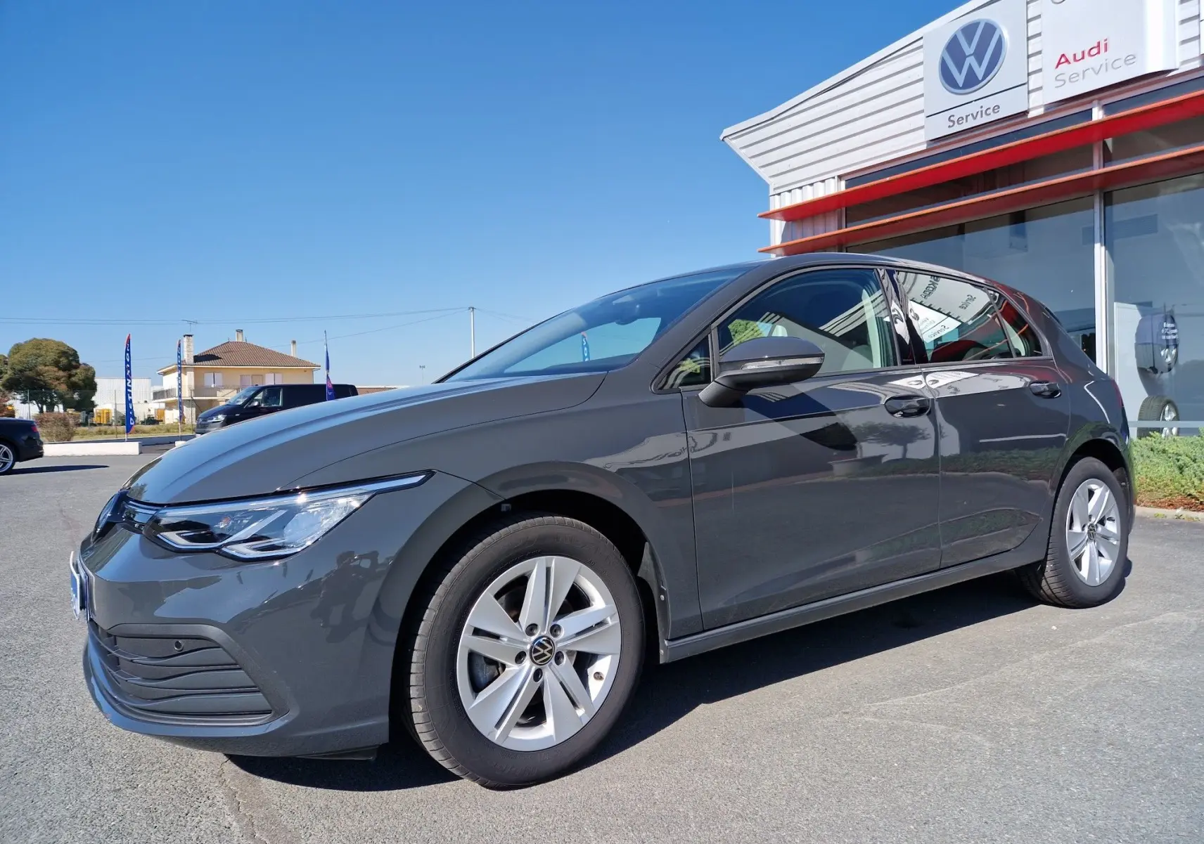 Volkswagen Golf A8 gris Urano vue 3/4 avant droit, avec jantes alliage et calandre moderne devant un service Volkswagen.