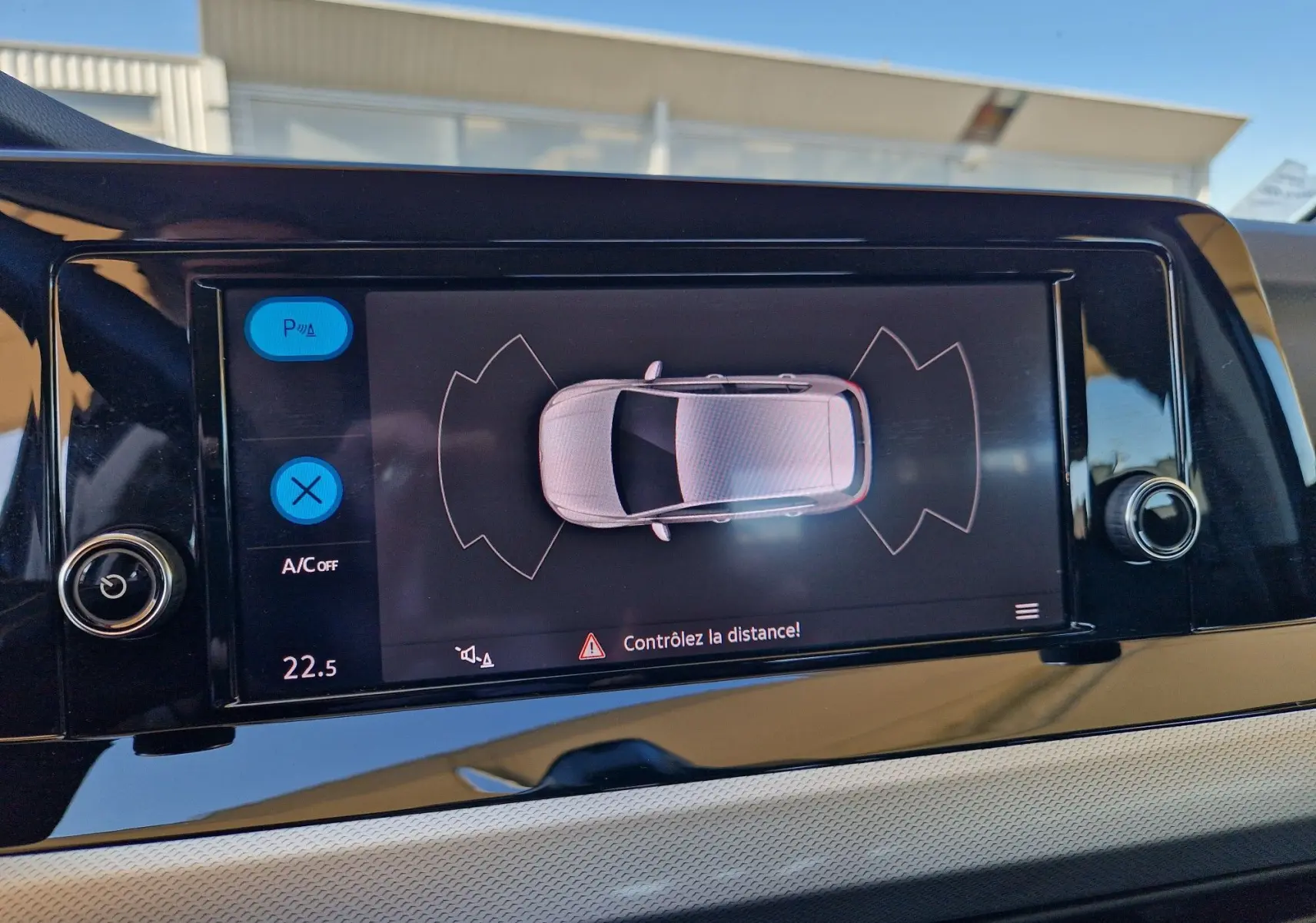 Écran central de la Volkswagen Golf A8 2023 montrant l'alerte de distance avec vue aérienne du véhicule gris Urano.