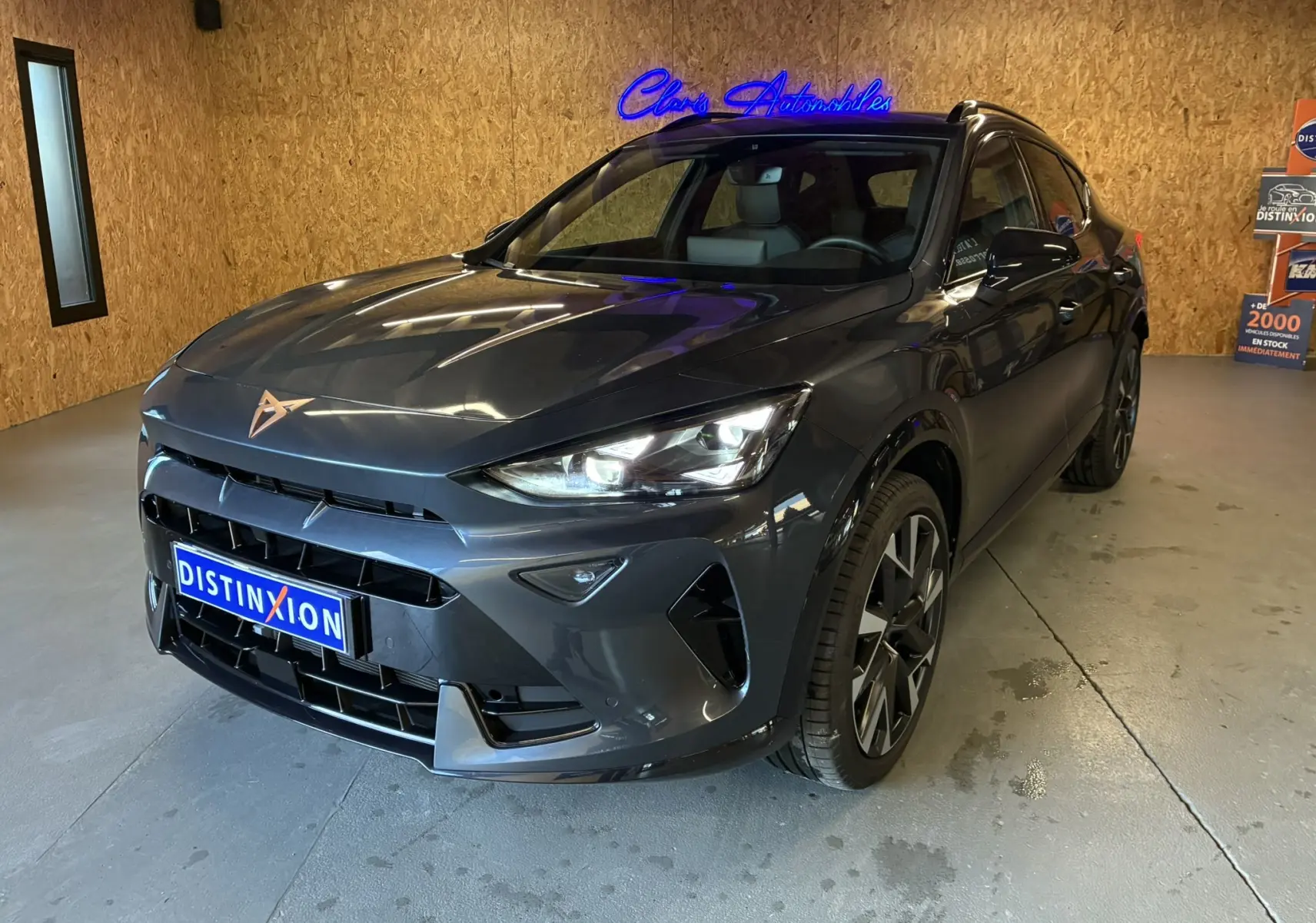 Vue 3/4 avant droite d'un CUPRA Formentor gris foncé 2024 avec phares LED et jantes bi-ton dans un showroom.