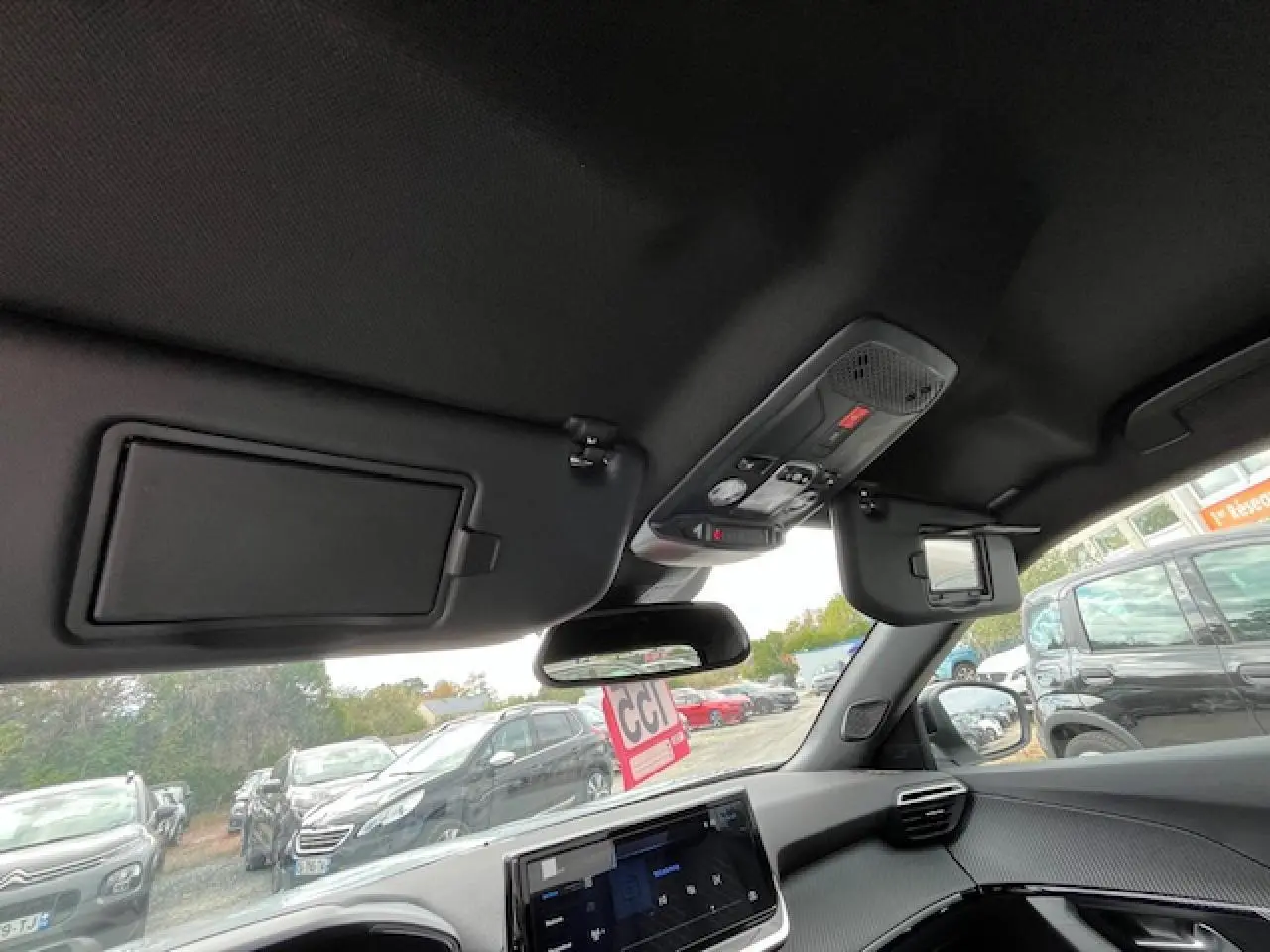 Vue intérieure avant du Peugeot 2008 blanc Okenite, montrant le tableau de bord et les pare-soleil avec miroirs intégrés.
