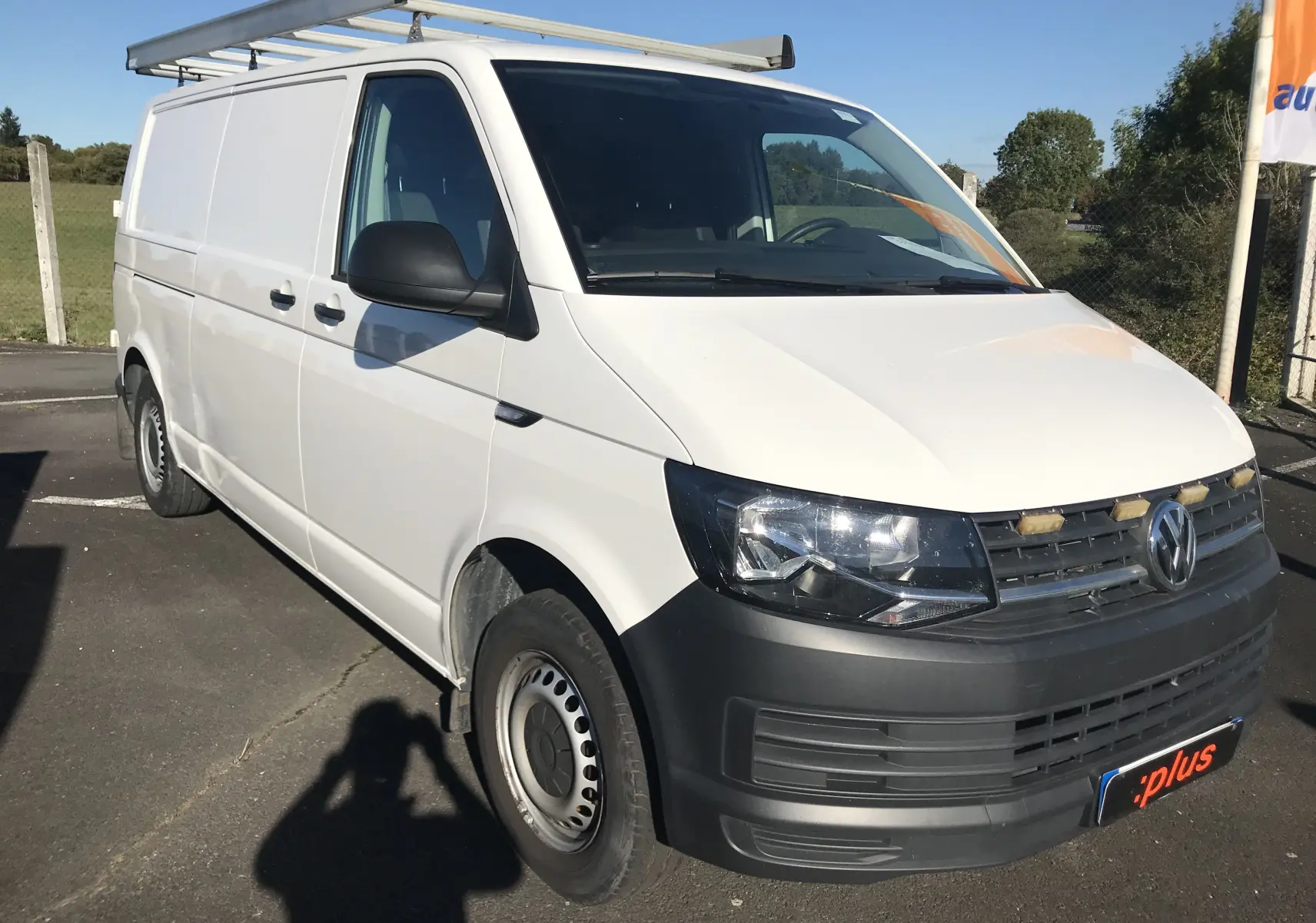 Volkswagen Transporter T6 blanc vu en 3/4 avant droit avec galerie de toit et pare-chocs noirs robustes.