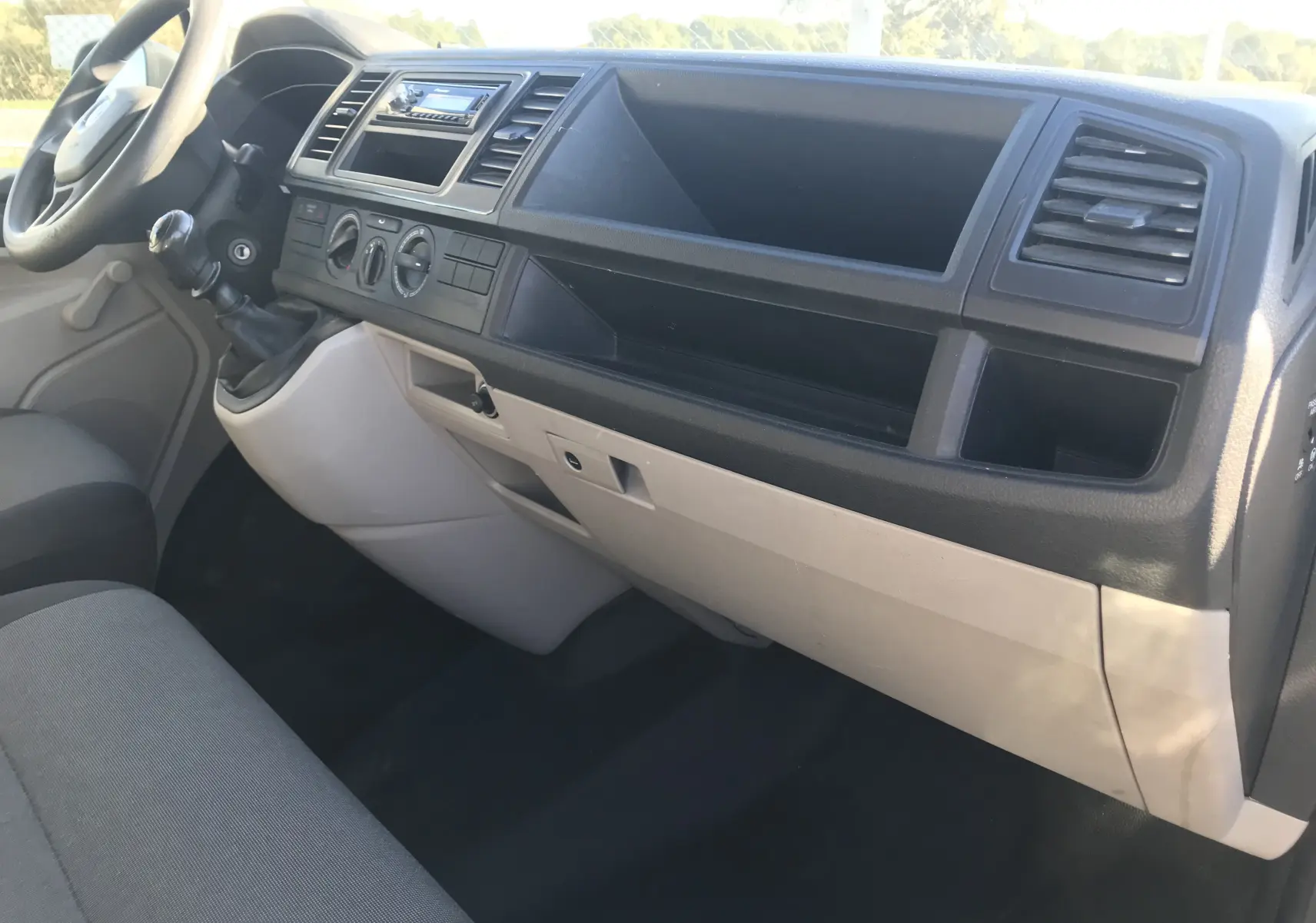 Intérieur du Volkswagen Transporter T6 L2 H1 2016, tableau de bord gris et beige vu côté passager avec levier de vitesses manuel.