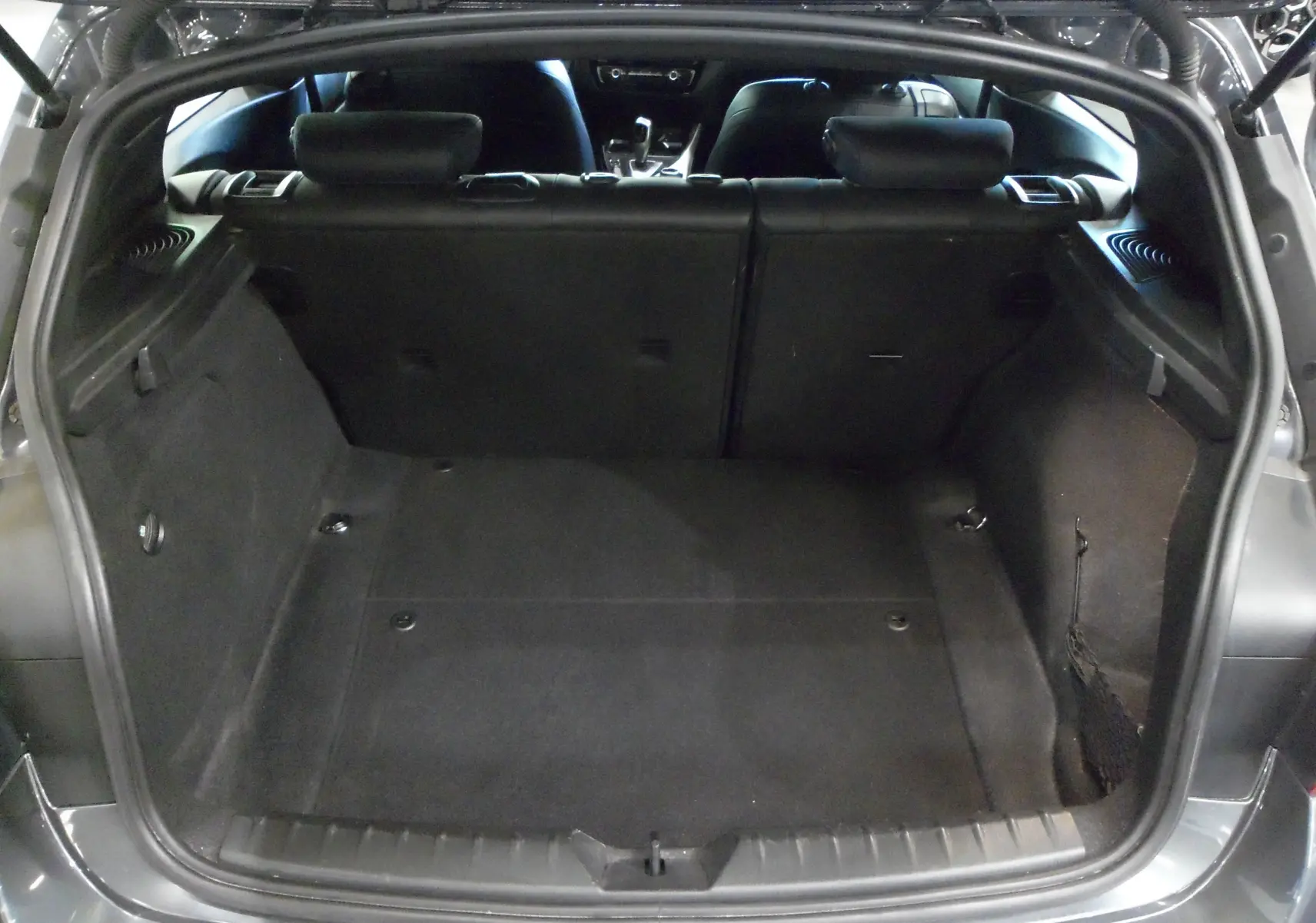 Coffre ouvert d'une BMW Série 1 F21 LCI gris, vue arrière montrant l'espace de chargement et l'intérieur noir.