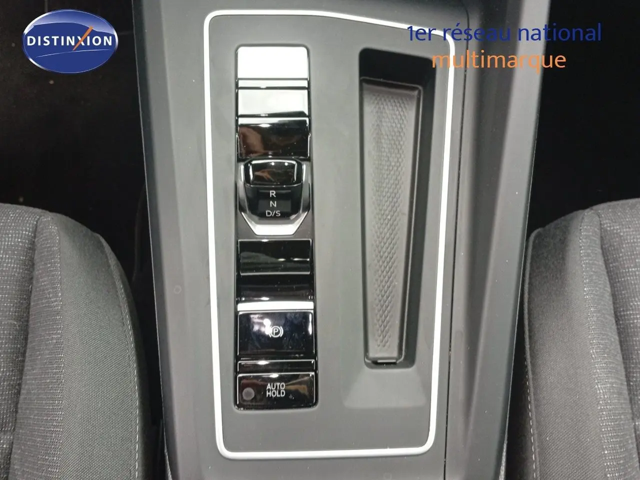 Vue en plongée sur la console centrale de la Volkswagen Golf VIII avec levier de vitesses automatique et sièges gris.