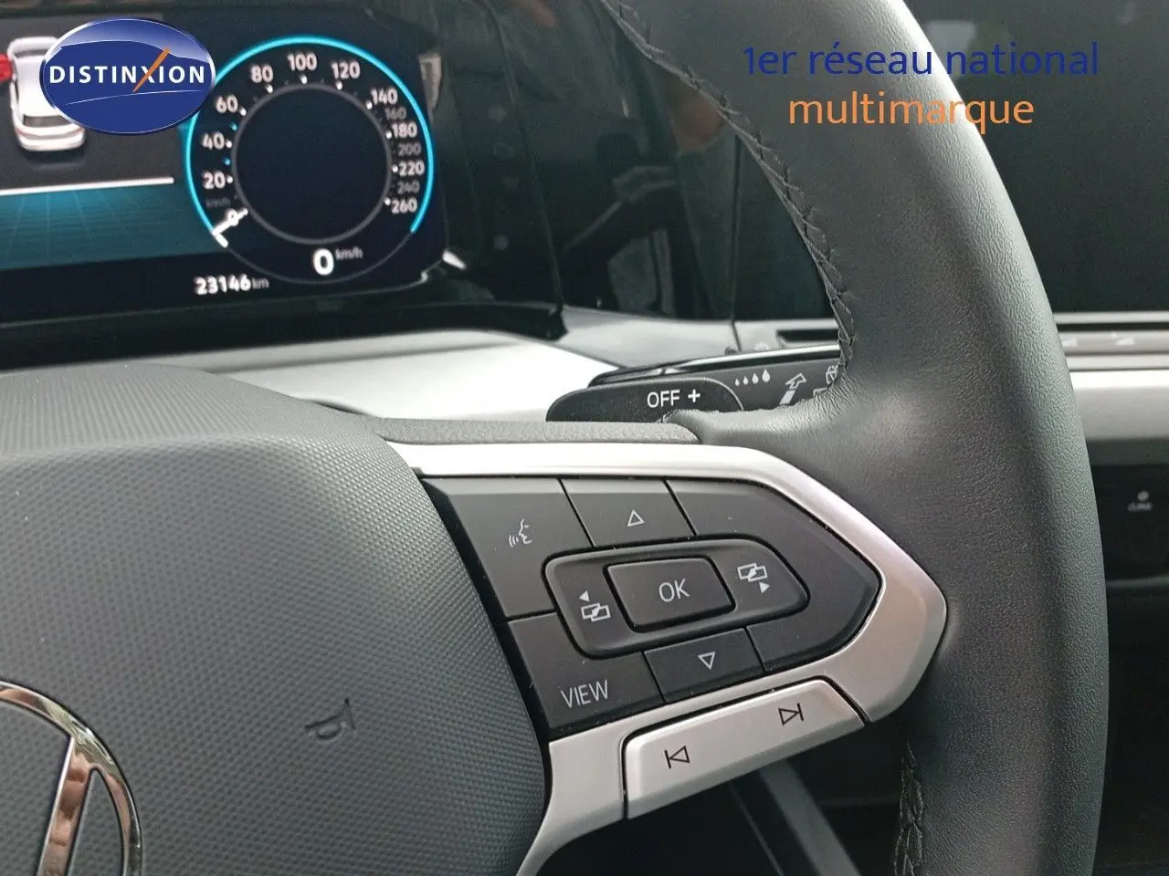 Gros plan sur le volant noir de la Volkswagen Golf VIII avec commandes multifonctions et tableau de bord numérique en arrière-plan.