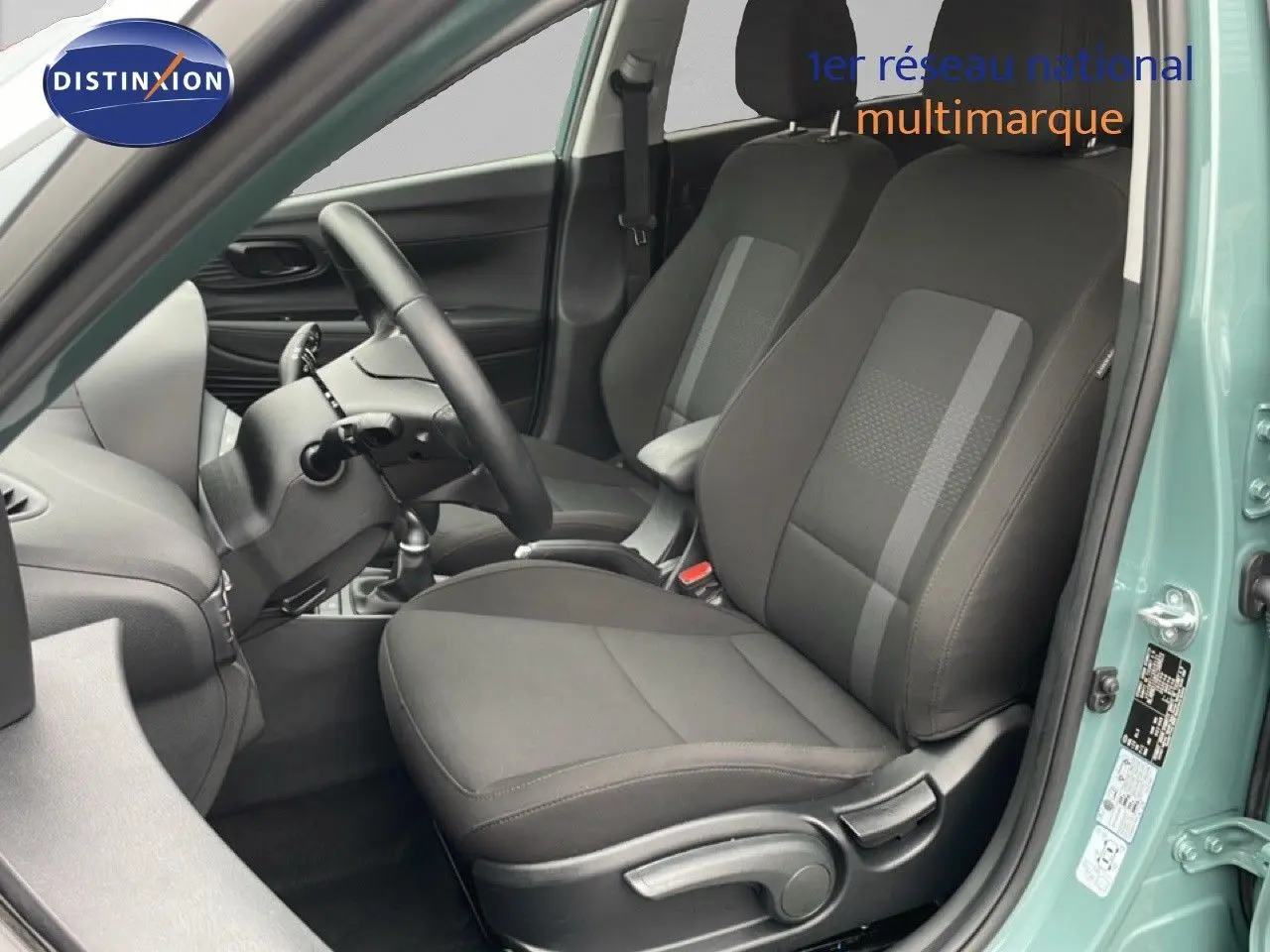 Vue intérieure côté conducteur de la Hyundai i20 2025 vert mangrove, sièges tissu noir et volant multifonction.