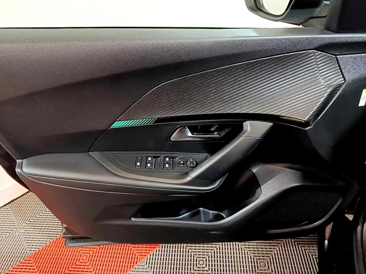Vue intérieure côté gauche de la porte avant d’un Peugeot 2008 noir avec insert effet carbone et commandes électriques.