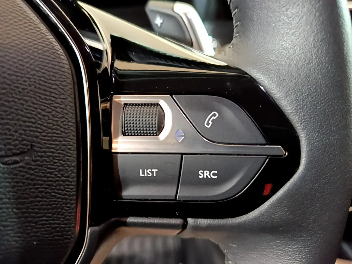 Gros plan sur les commandes multifonctions noires du volant cuir du Peugeot 2008 noir, version BlueHDi 130.