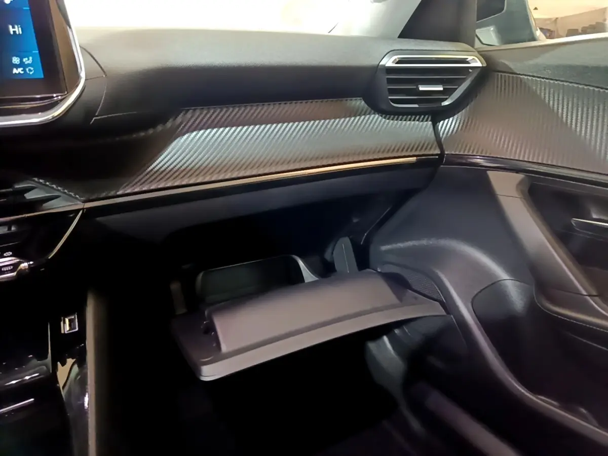 Intérieur côté passager du Peugeot 2008 2021 noir, montrant la boîte à gants ouverte et le tableau de bord avec finition carbone.