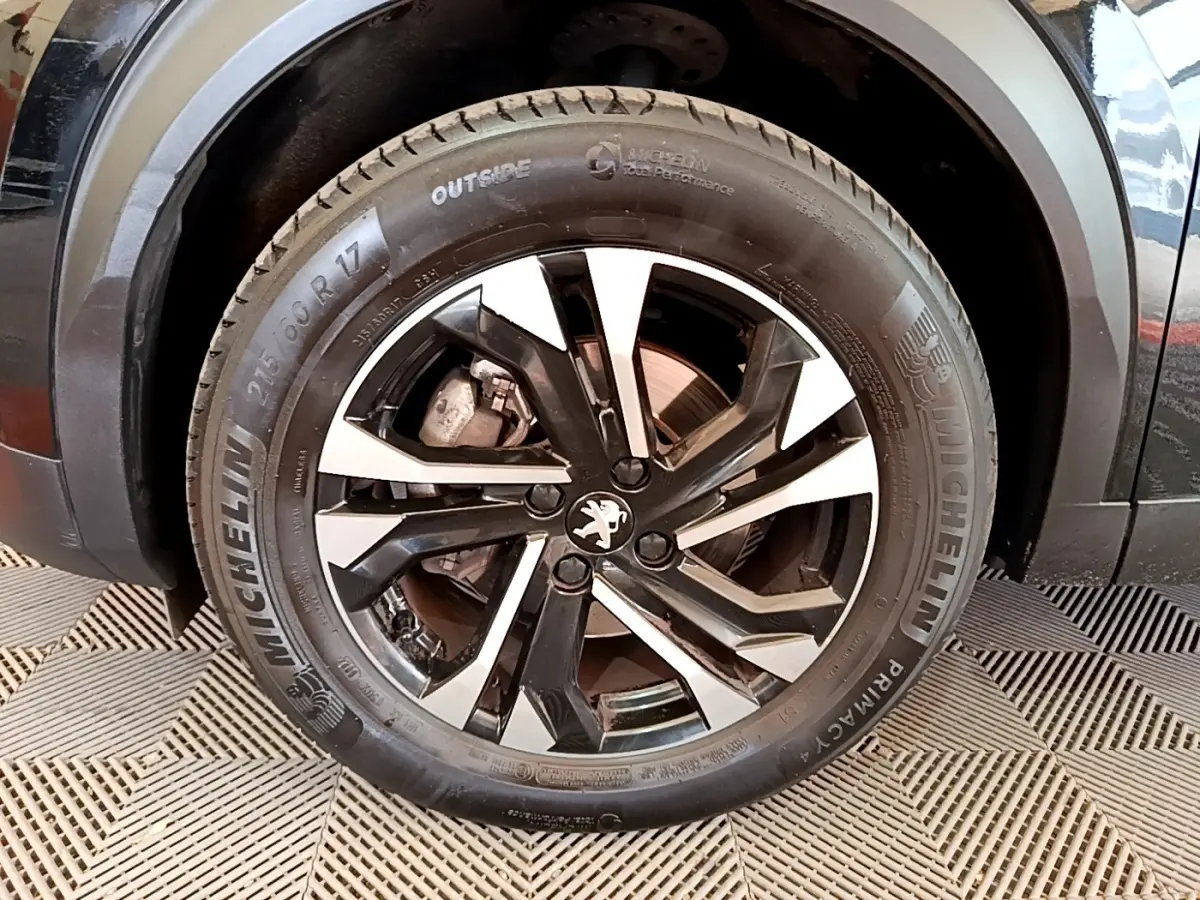 Gros plan sur la roue avant gauche noire d’un Peugeot 2008 2021 avec jante alliage bicolore et pneu Michelin.