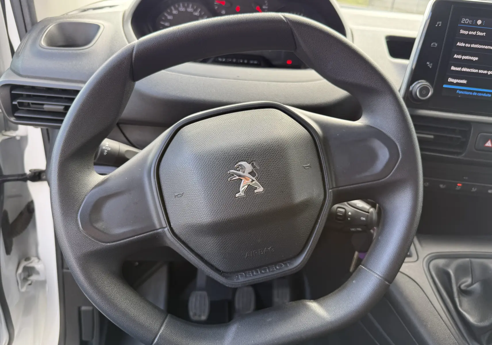 Volant noir de Peugeot Partner 2021 vu de face, avec tableau de bord et écran tactile en arrière-plan.