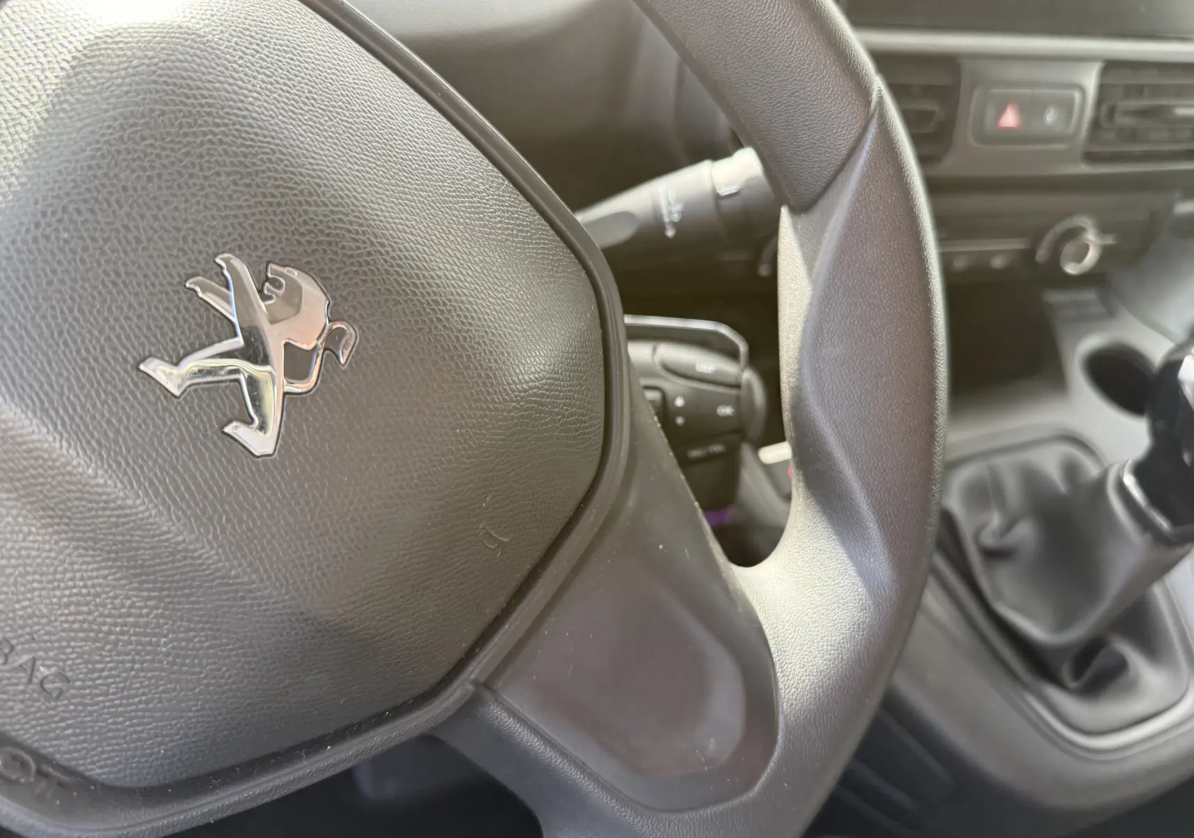 Gros plan sur le volant Peugeot noir et la boîte manuelle du Partner blanc, mettant en valeur l'intérieur fonctionnel du véhicule.