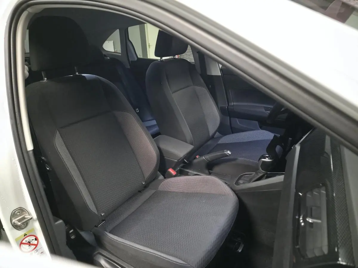 Vue intérieure côté conducteur du Volkswagen Taigo blanc 2024, sièges en tissu gris et console centrale avec levier de vitesse.