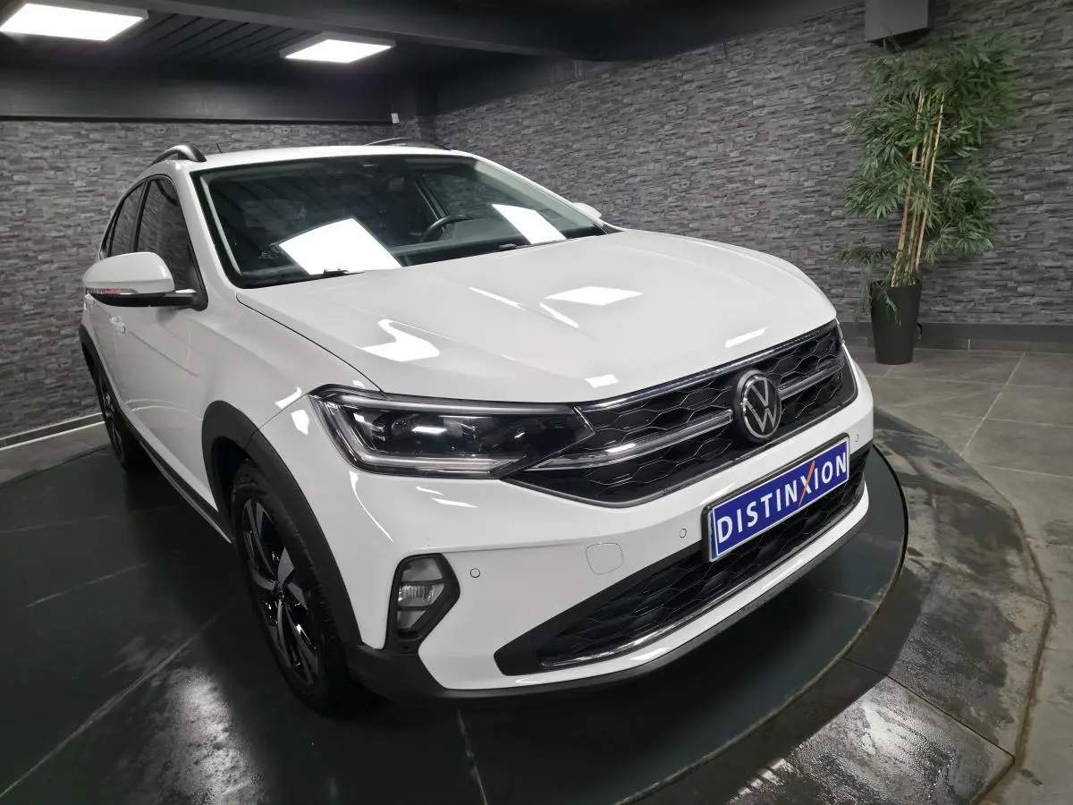 Vue 3/4 avant droite du Volkswagen Taigo blanc avec calandre noire et projecteurs LED dans un showroom.