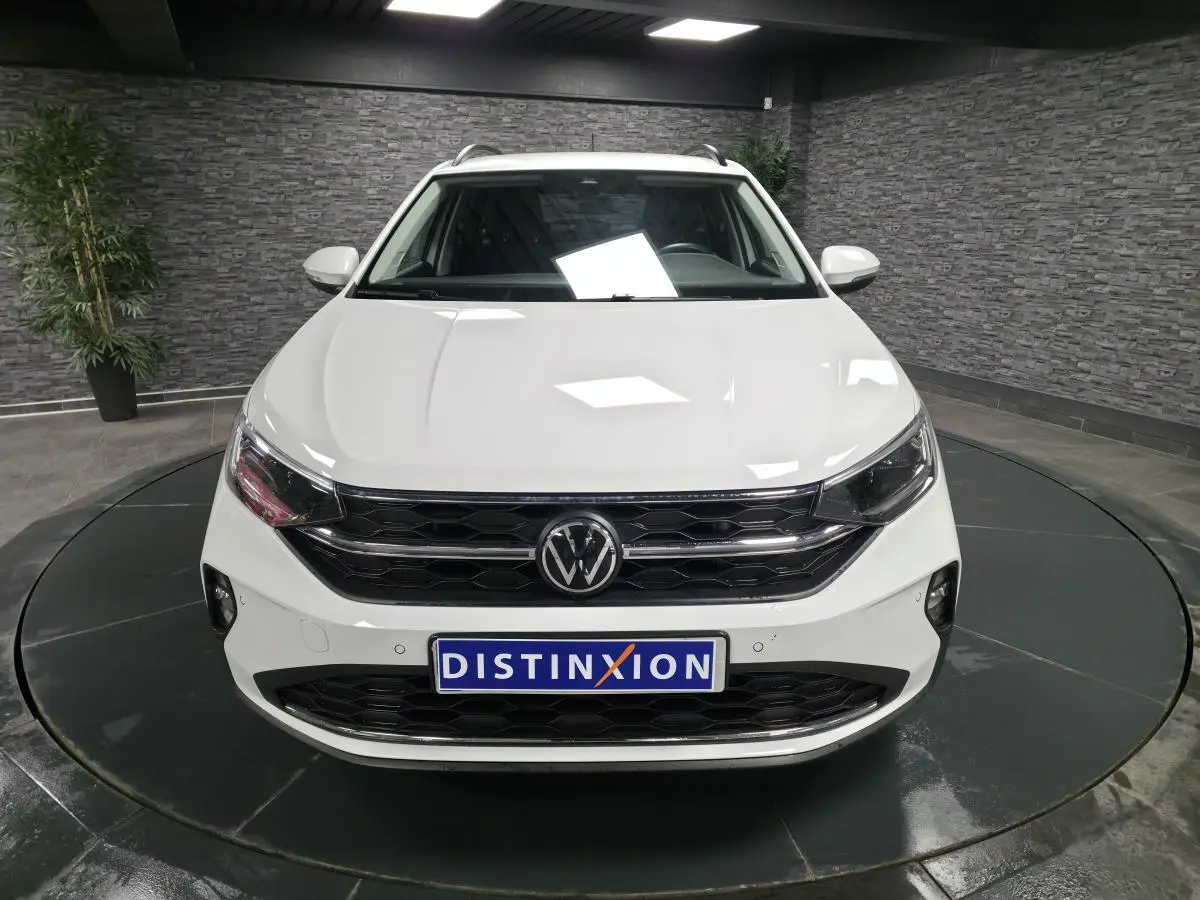 Vue frontale d'un Volkswagen Taigo blanc avec calandre noire et logo VW centré, en showroom intérieur.