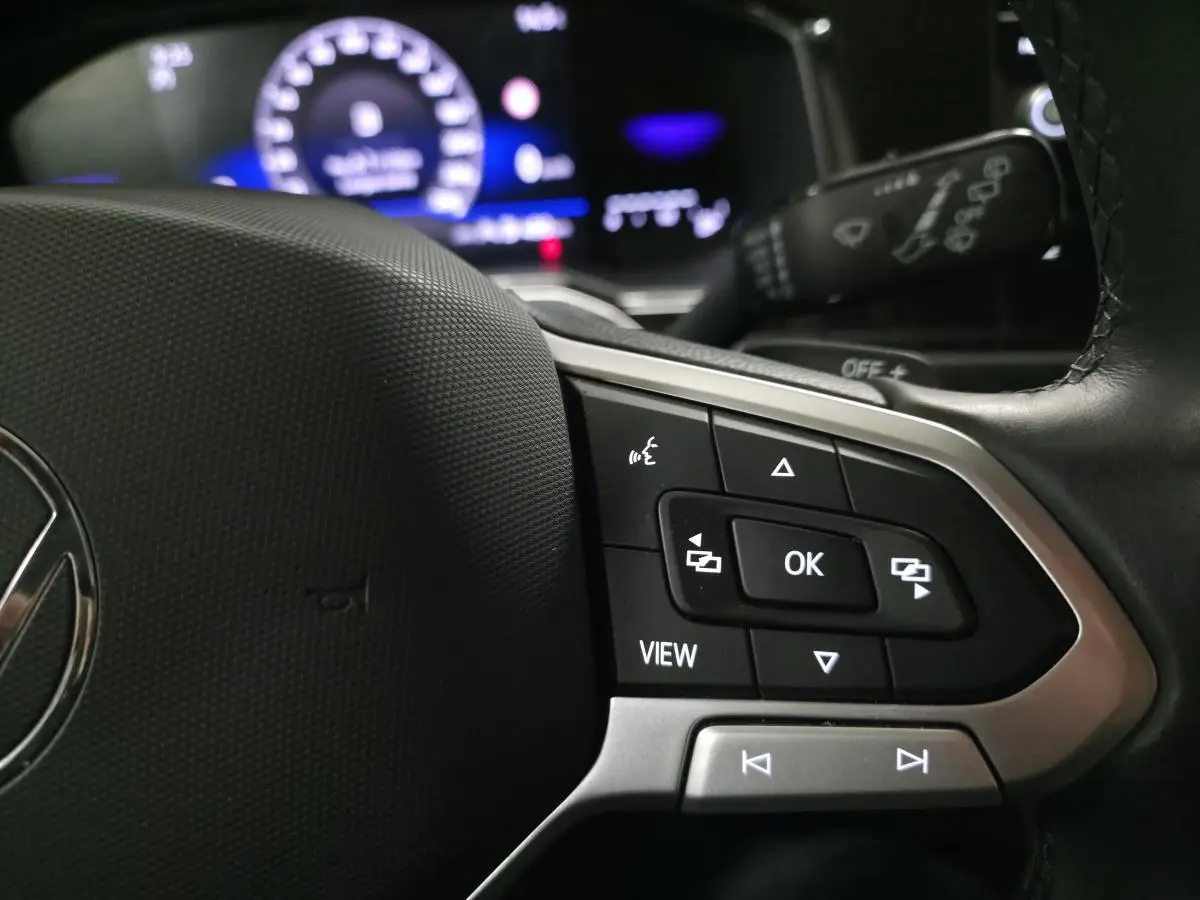 Gros plan sur les commandes multifonctions du volant cuir du Volkswagen Taigo 2024 avec affichage digital en arrière-plan.